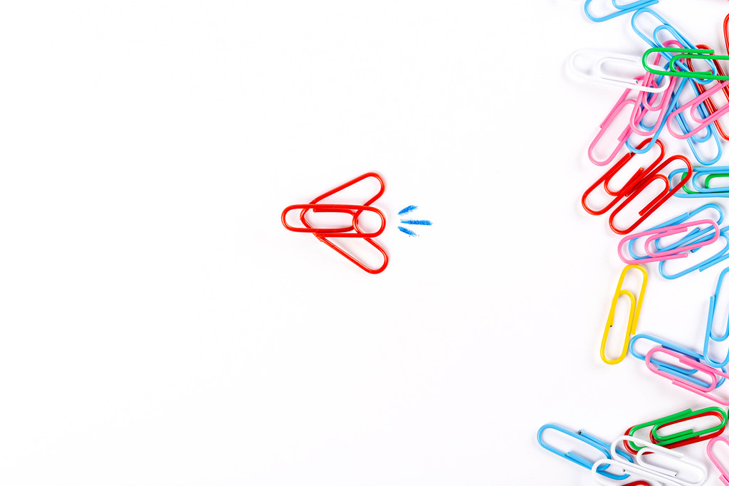 Many multicolored paper clips and plane made of paper clips on white