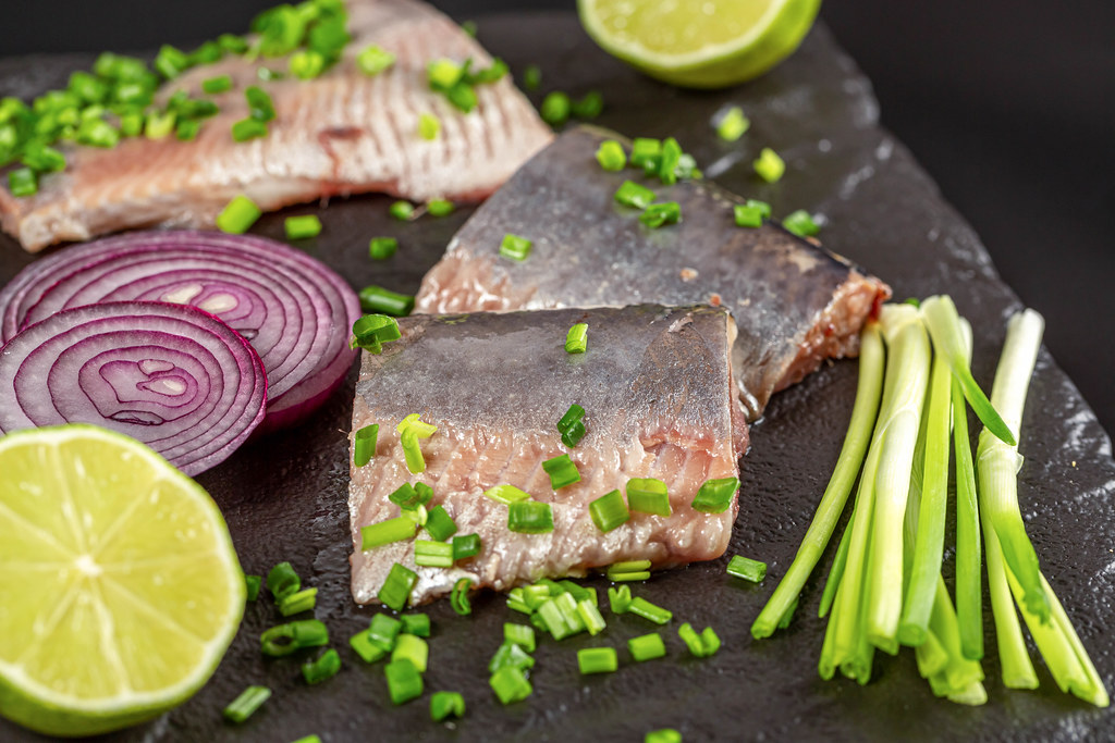 Marinated herring fillet with lime, green and purple onions on black, close-up