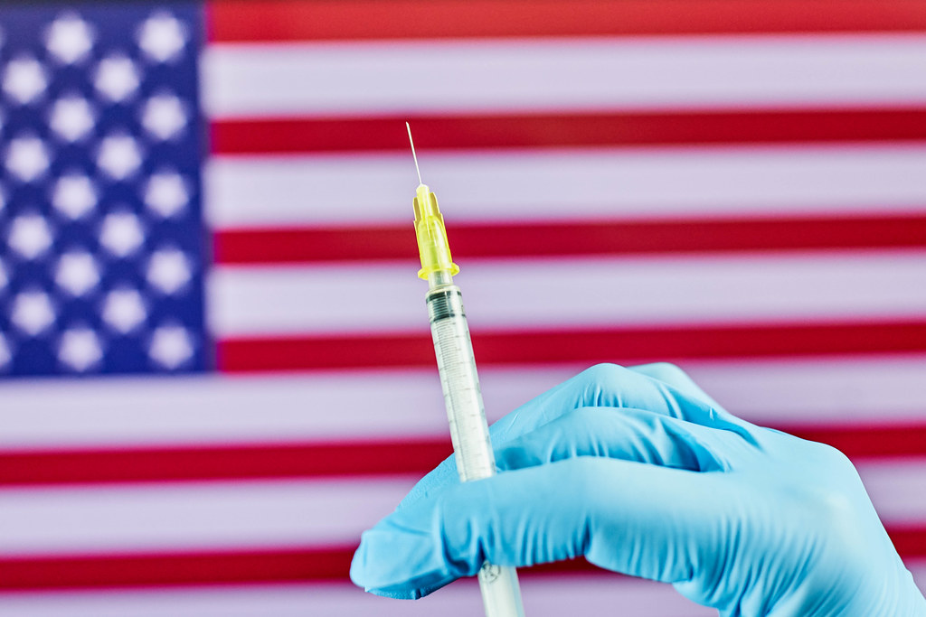Mass vaccination in the US. Doctor hold syringe against the American flag