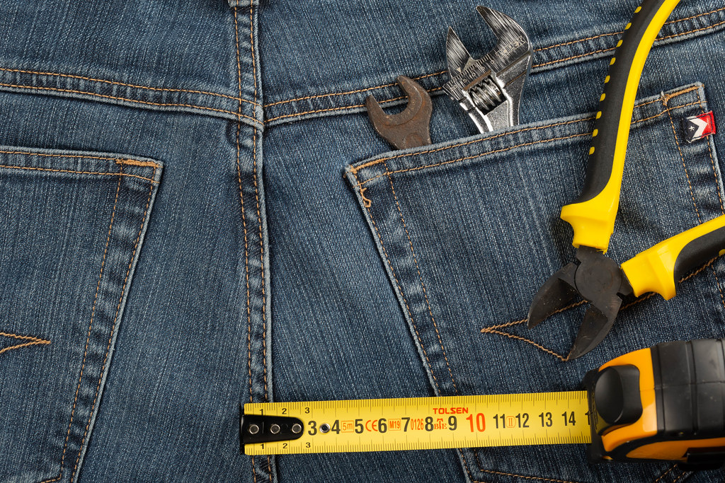 Measuring tape, wire cutters and wrenches on jeans background
