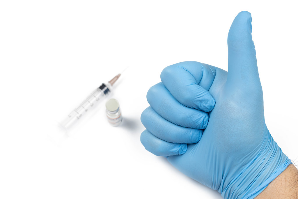 Medical Blue glove on the hand with Thumb up and Vaccine in the background