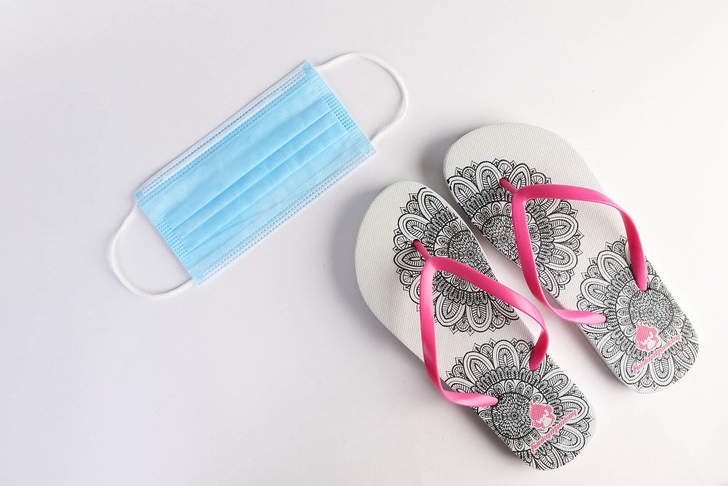 Medical face mask and flipflops on white background