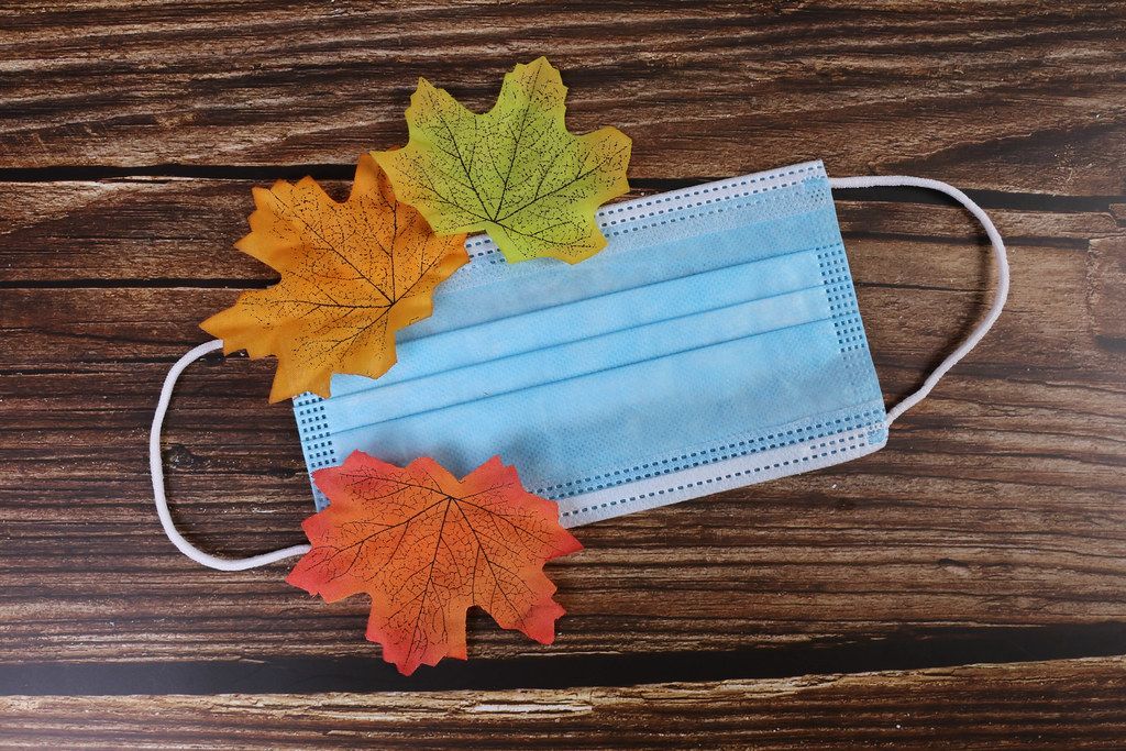 Medical face mask with autumn leaves on wooden background