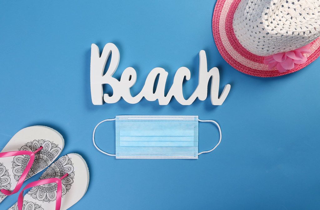 Medical face mask with flipflops, sun hat and Beach text on blue background