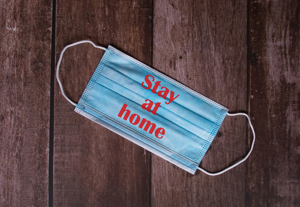 Medical face mask with Stay at Home text on wooden background