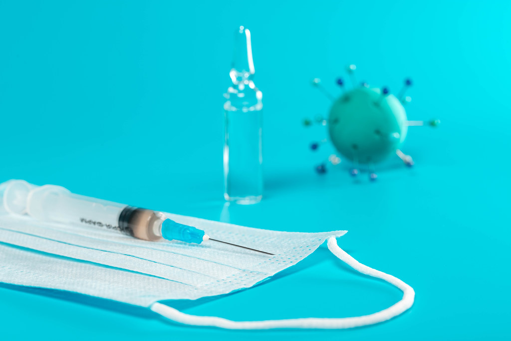 Medical mask with syringe, ampoule and abstract virus model on blue background