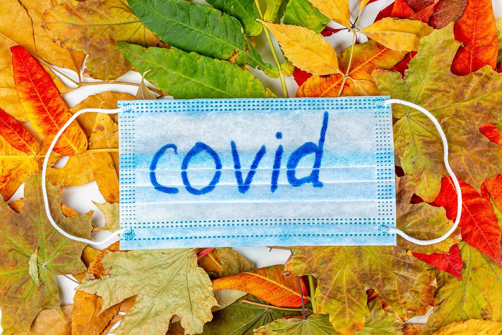 Medical mask with the inscription Covid-19 on dry autumn leaves