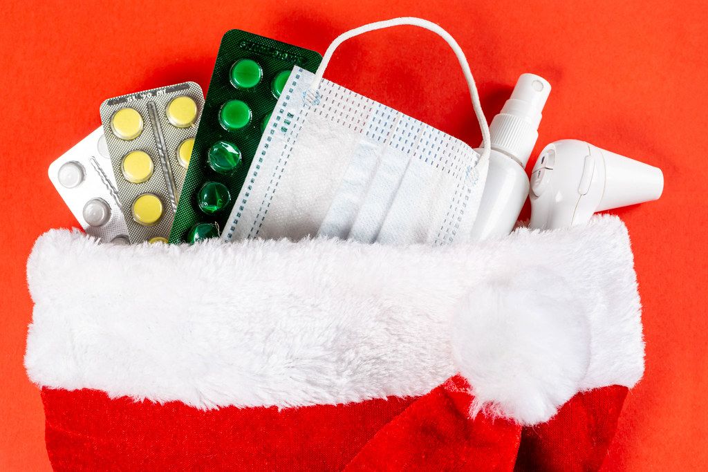 Medical pills, electric thermometer and disposable mask in santa hat on red background