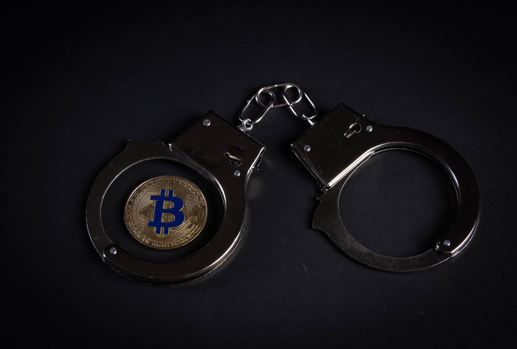 Metal handcuffs and Bitcoin coin on black background