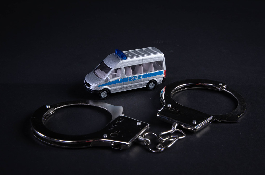 Metal handcuffs and police car on black background