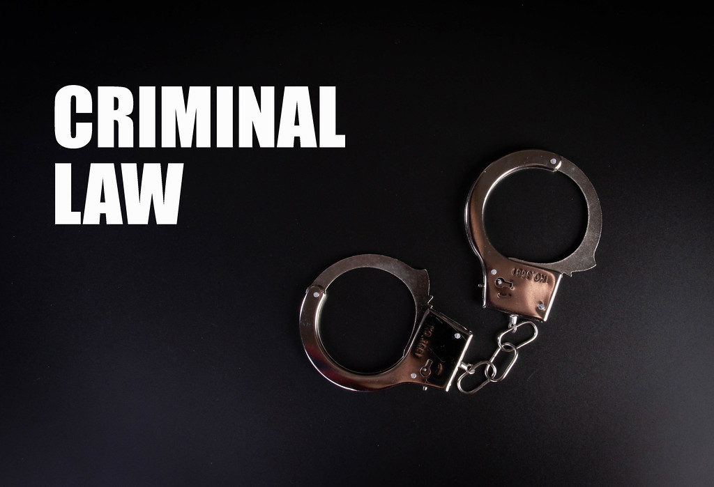 Metal handcuffs on black background with Criminal Law text