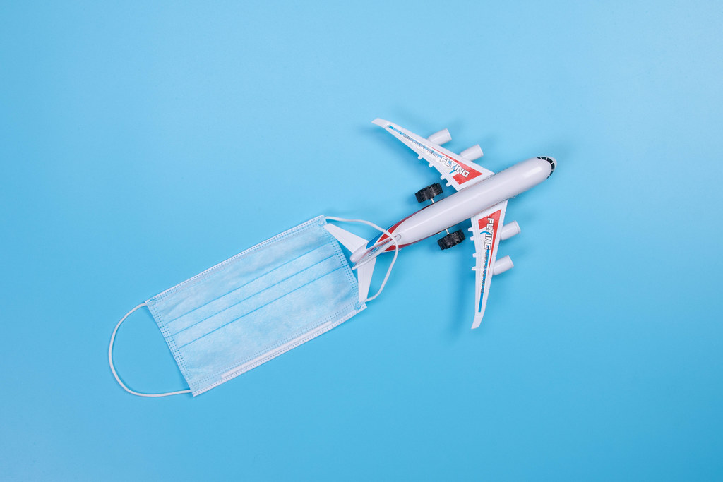 Miniature airplane with medical face mask on blue background