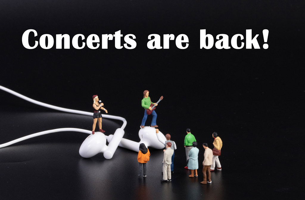 Miniature band with earbuds on black background and concerts are back text
