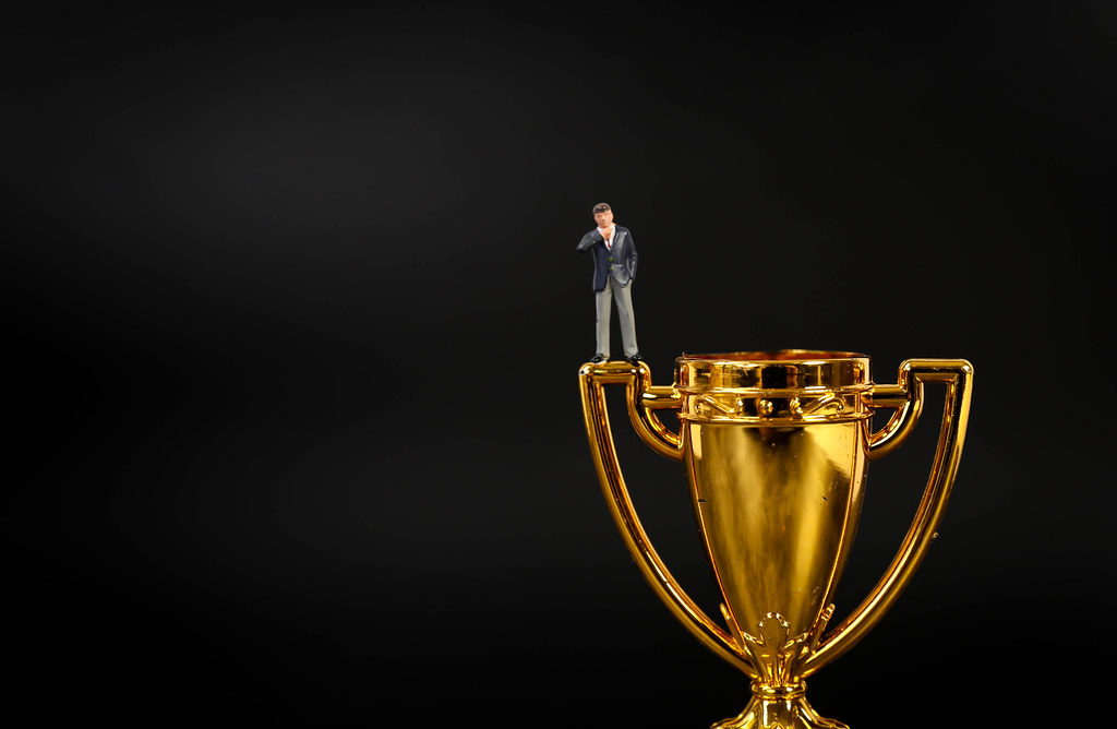 Miniature businessman on golden trophy