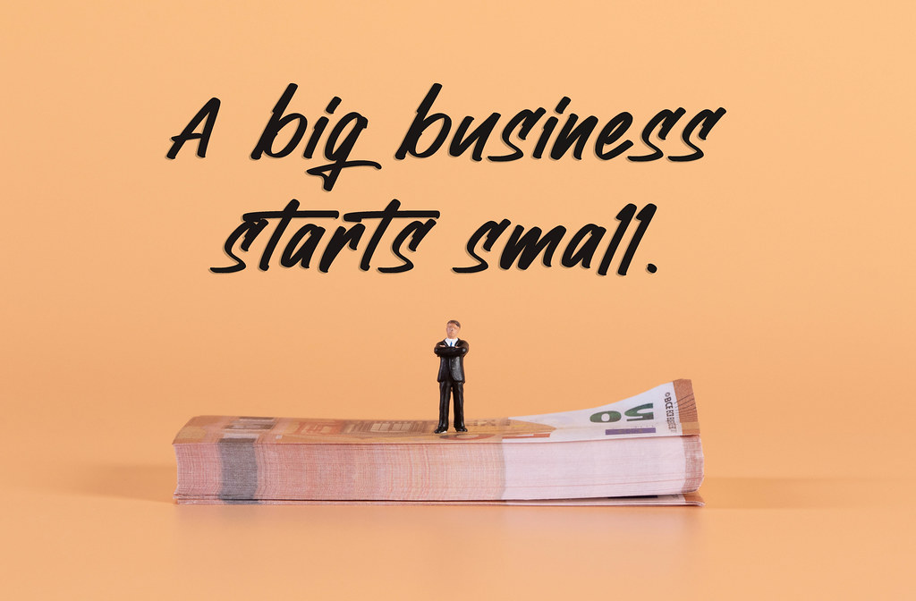 Miniature businessman standing on a stack of Euro money with A big business starts small text