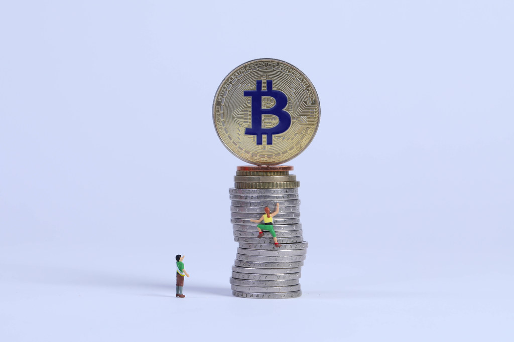 Miniature climber climbing on coin stack to Bitcoin coin