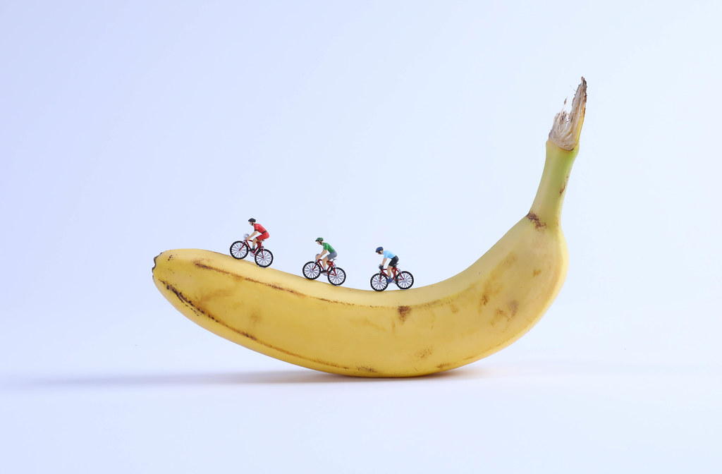 Miniature cyclists on banana on white background