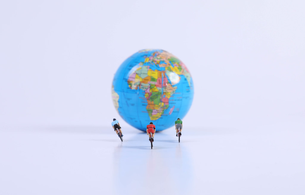Miniature figures ride bicycle in front of globe