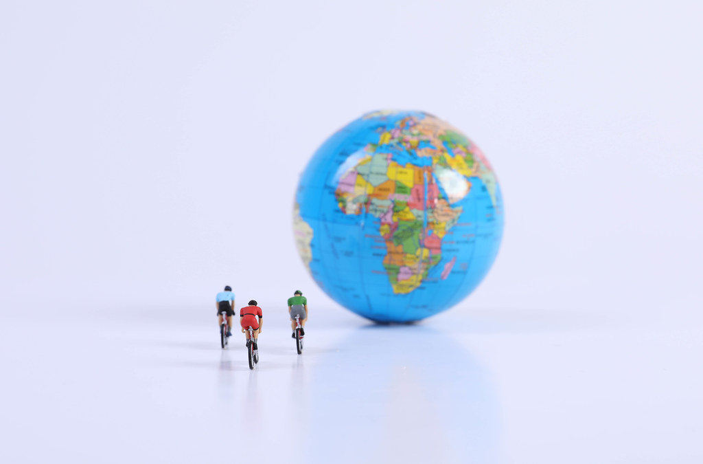 Miniature figures ride bicycle with globe on white background