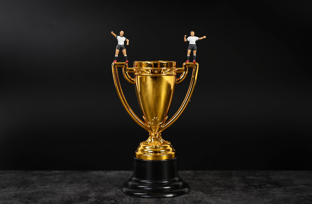 Miniature football players standing on golden trophy