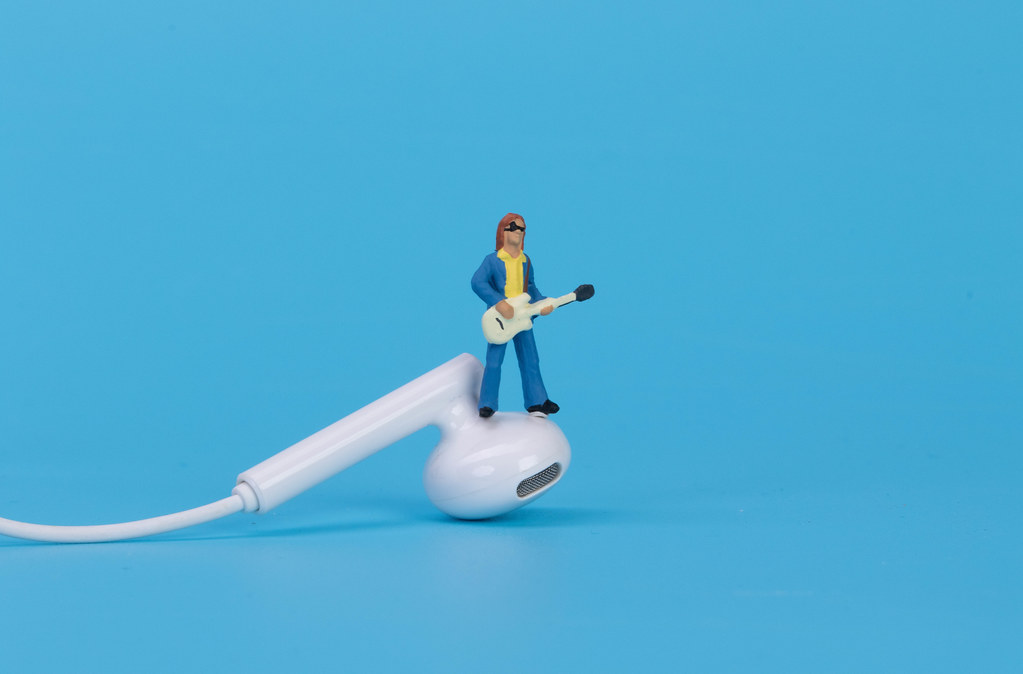 Miniature guitar player standing on pair of earbuds on blue background