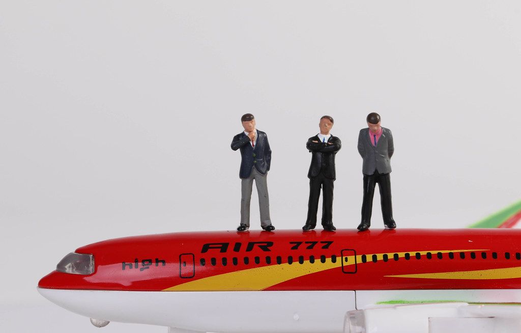 Miniature people businessman in suit and tie standing on toy airplane