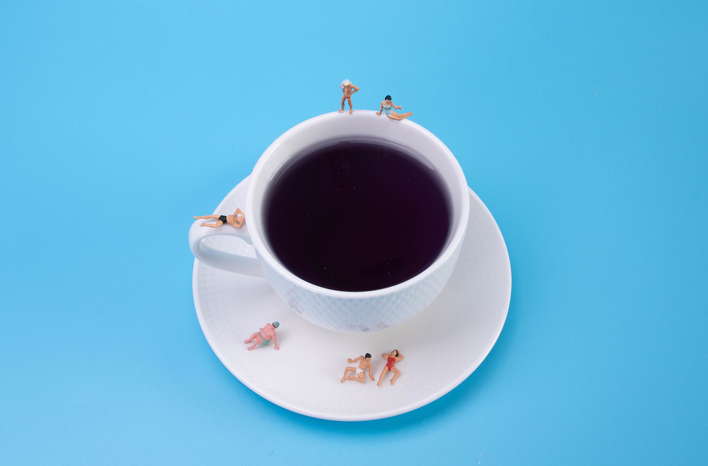 Miniature people relaxing around the coffee cup on blue background