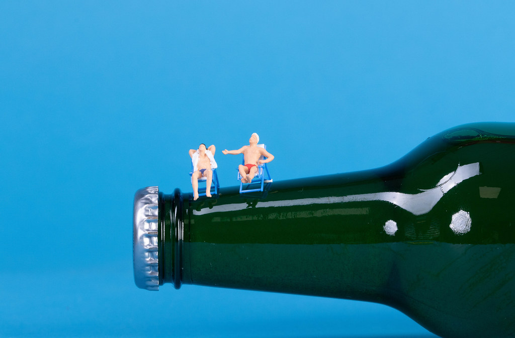 Miniature people relaxing in deck chairs on beer bottle