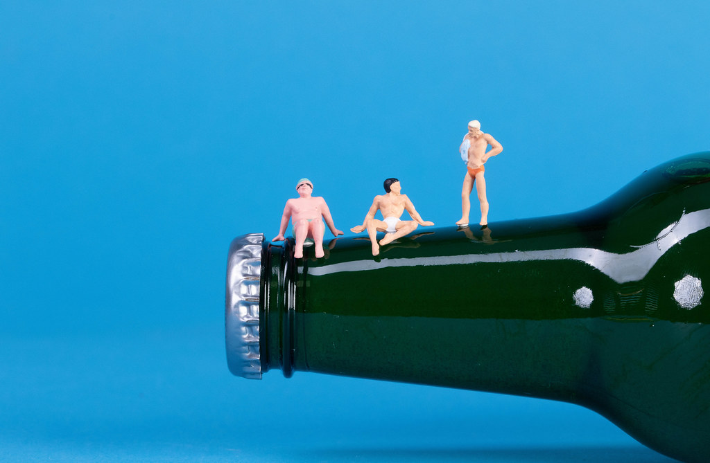 Miniature people relaxing on a beer bottle