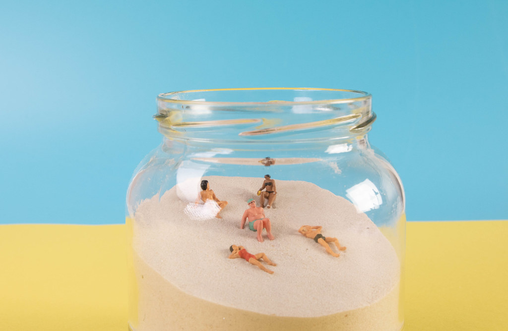 Miniature people relaxing on the sand in glass jar
