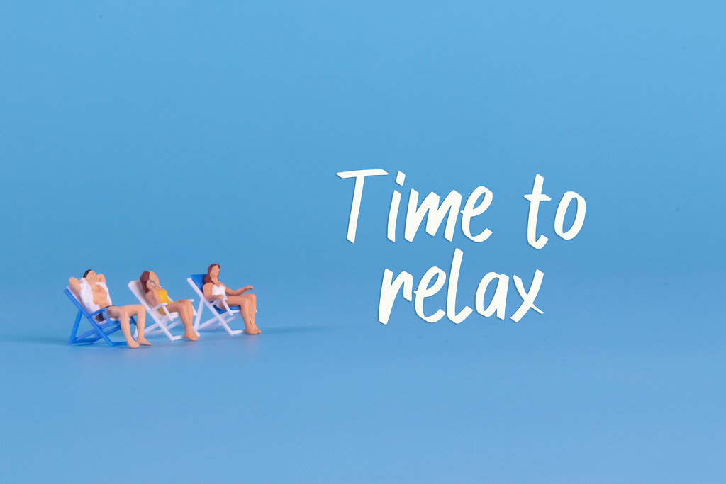 Miniature people sitting in deckchairs and Time to relax text