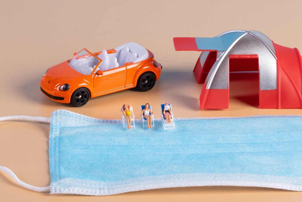 Miniature people sunbathing in deckchairs with face mask and camping tent