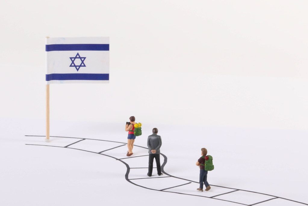 Miniature people walking on a path to the flag of Israel