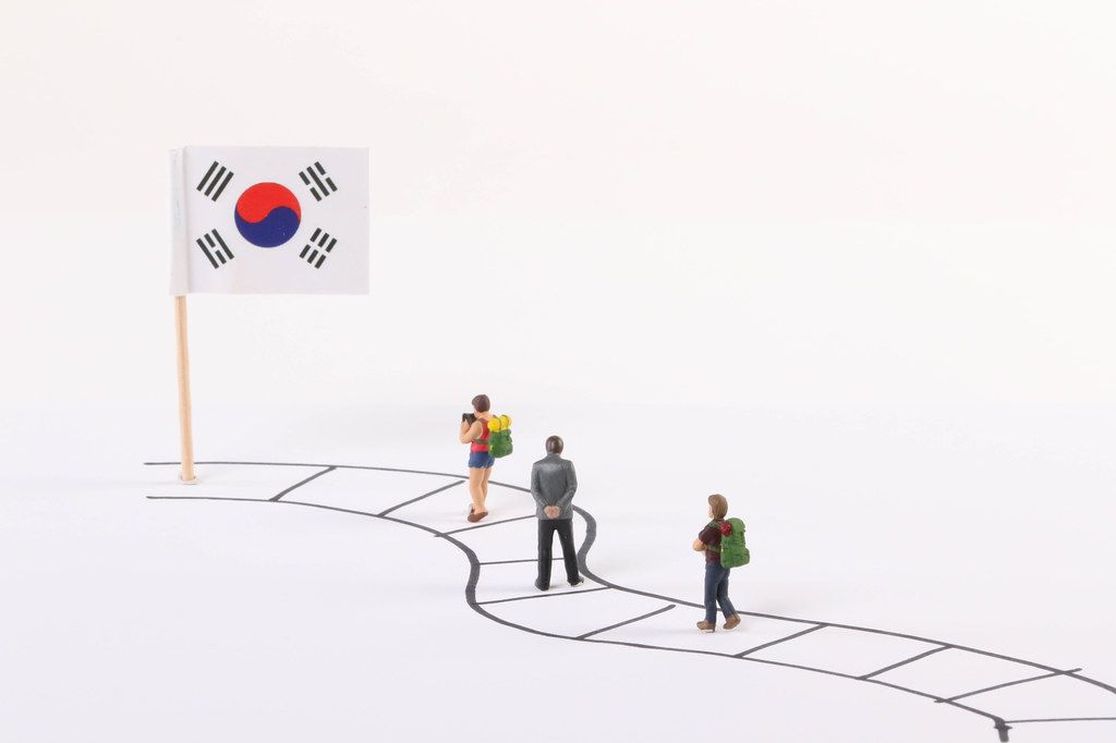 Miniature people walking on a path to the flag of South Korea
