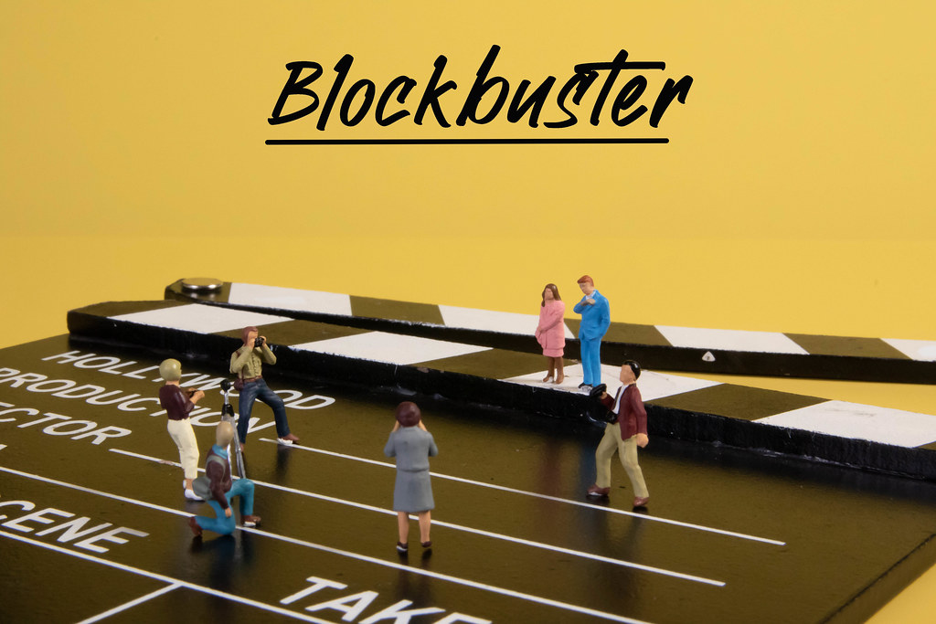 Miniature people with cameras on movie clapper and Blockbuster text