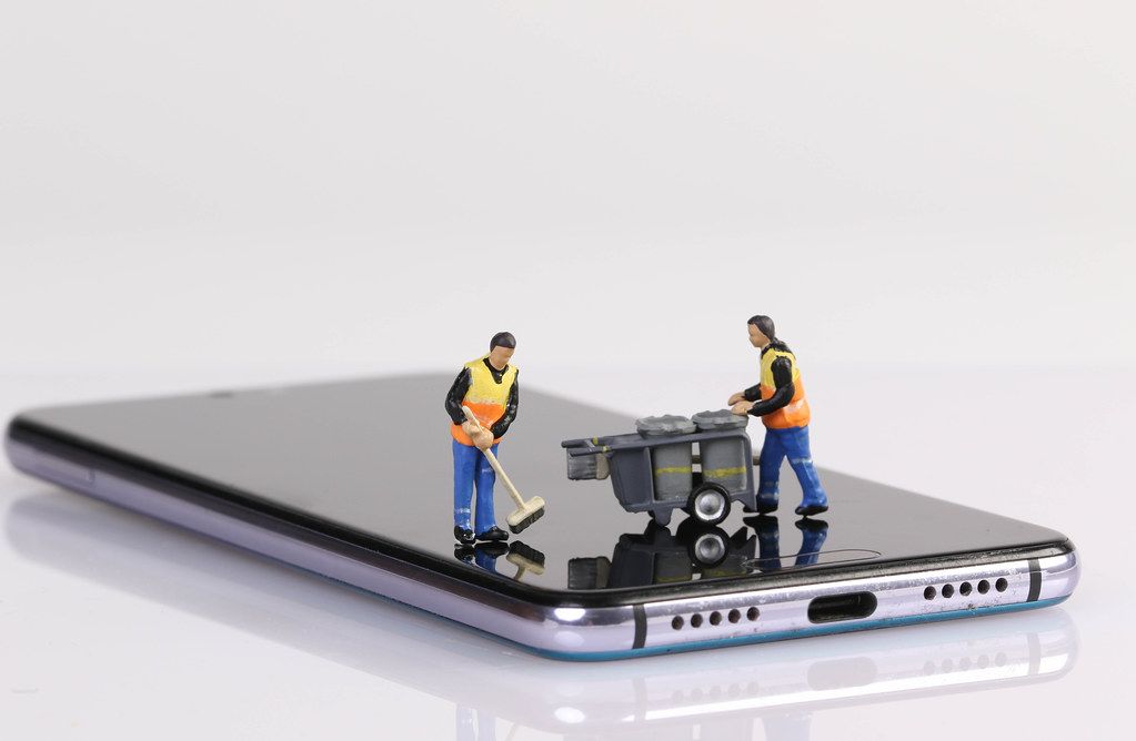 Miniature people workers cleaning smartphone screen on white background
