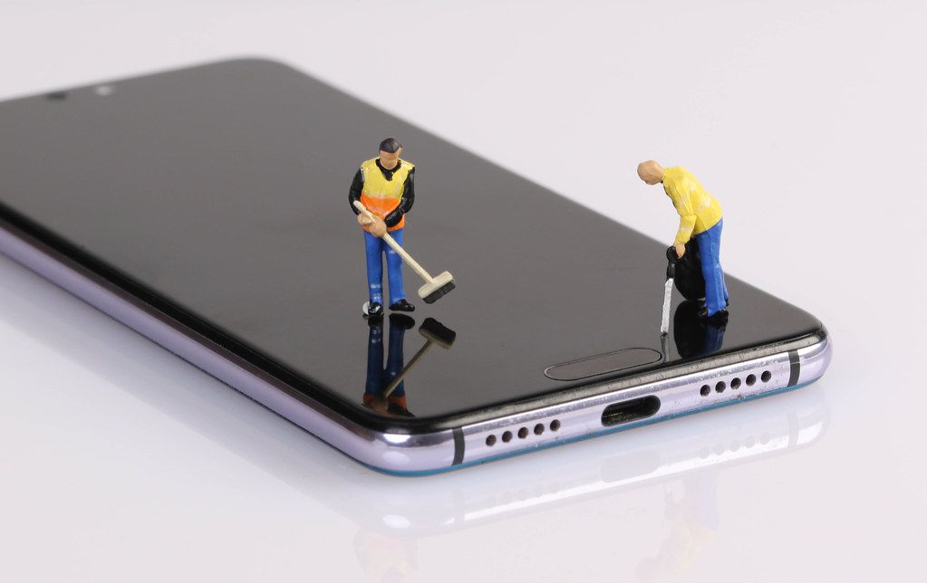 Miniature people workers cleaning smartphone screen