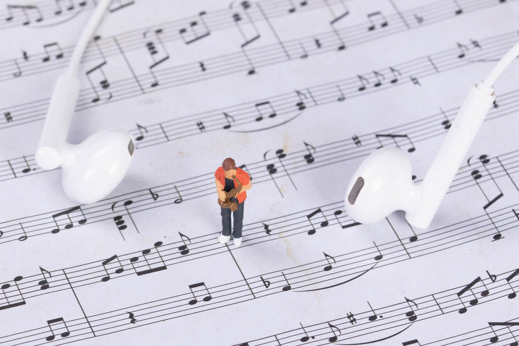 Miniature saxofonist with earbuds on music notes