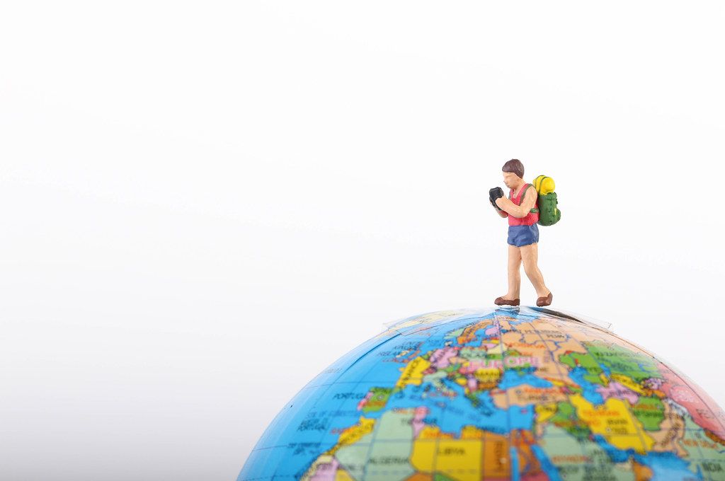 Miniature traveler with backpack on globe