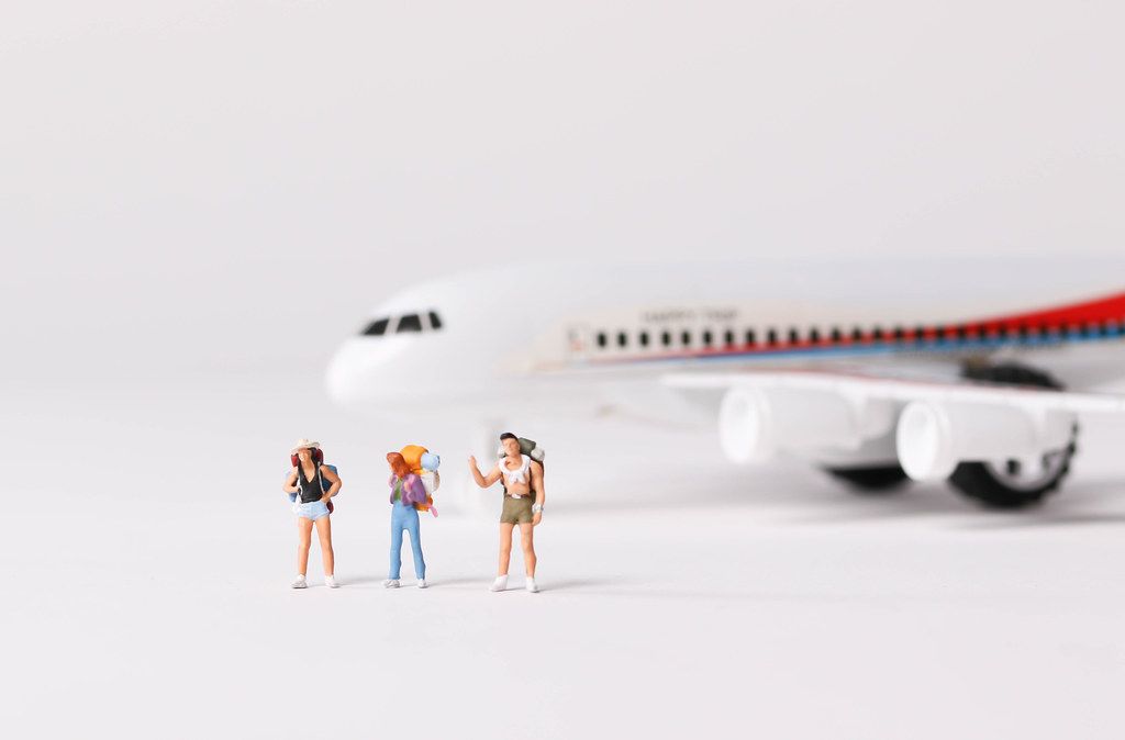 Miniature travelers and toy airplane on white background