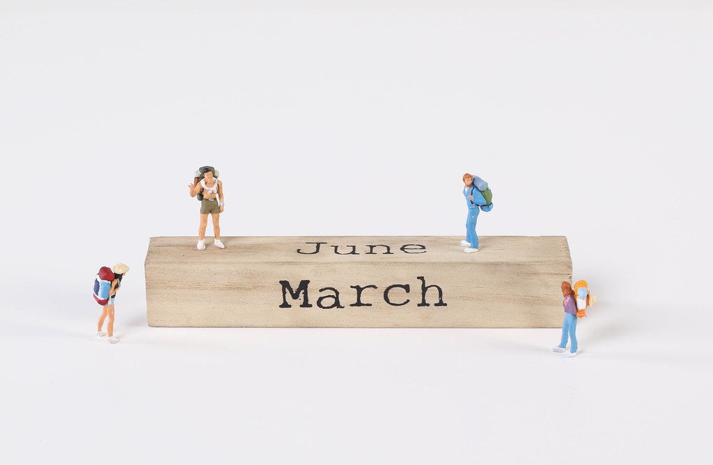 Miniature travelers and wooden block with June and March text on white background