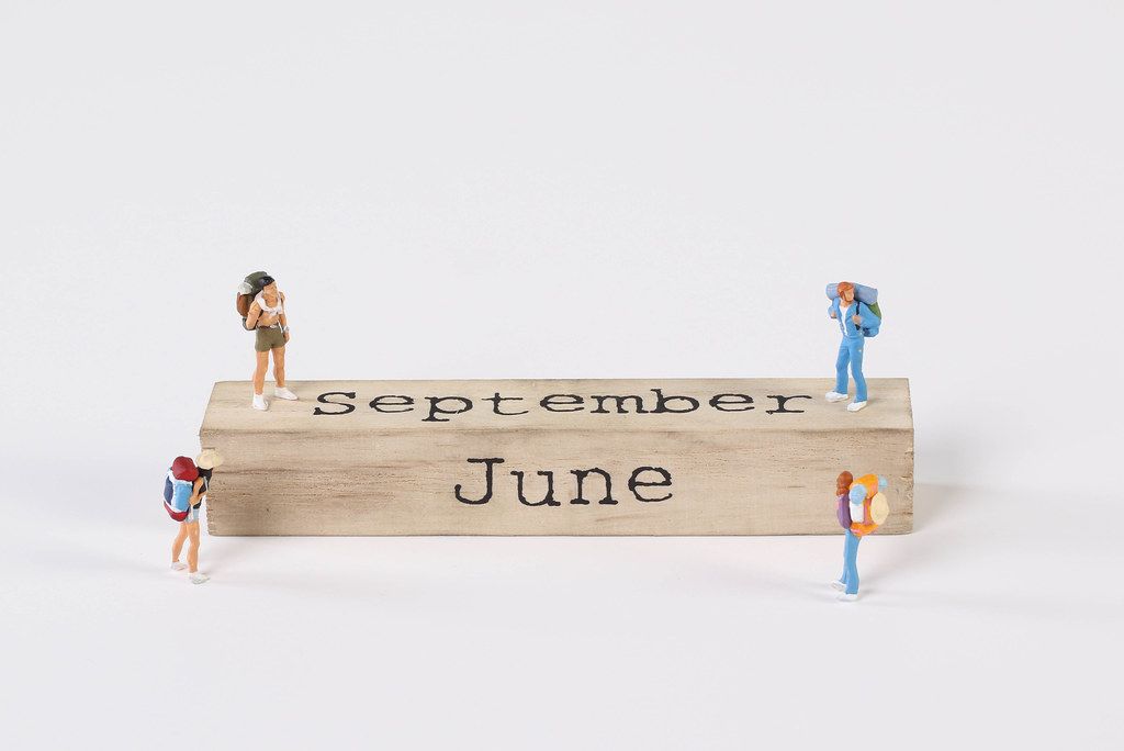Miniature travelers and wooden block with September and June text on white background