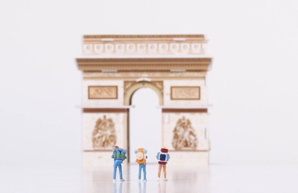 Miniature travelers stading in front of the The Arc de Triomphe