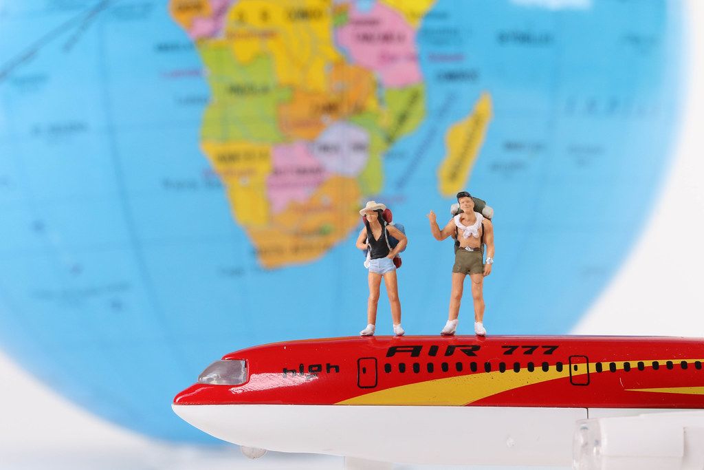 Miniature travelers standing on a red airplane with globe in the background