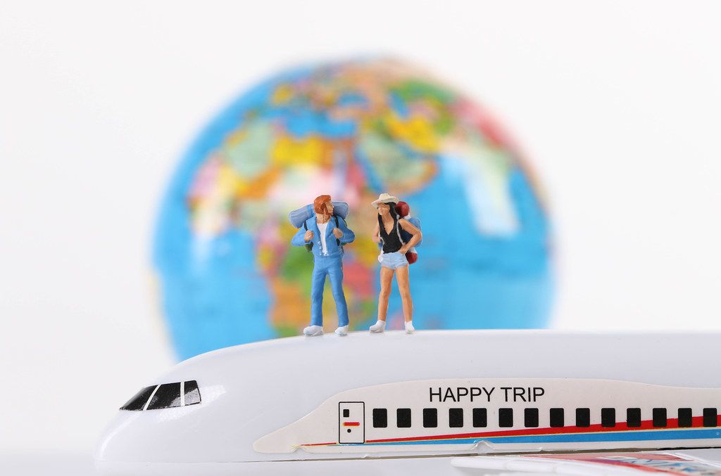Miniature travelers standing on airplane with globe in the background