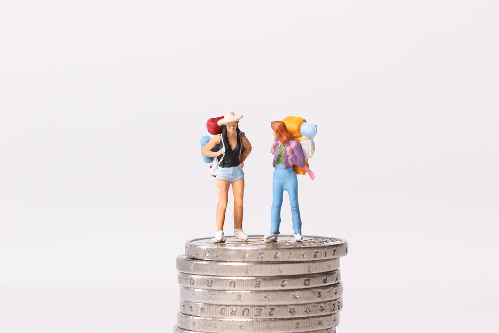 Miniature travelers standing on stack of coins