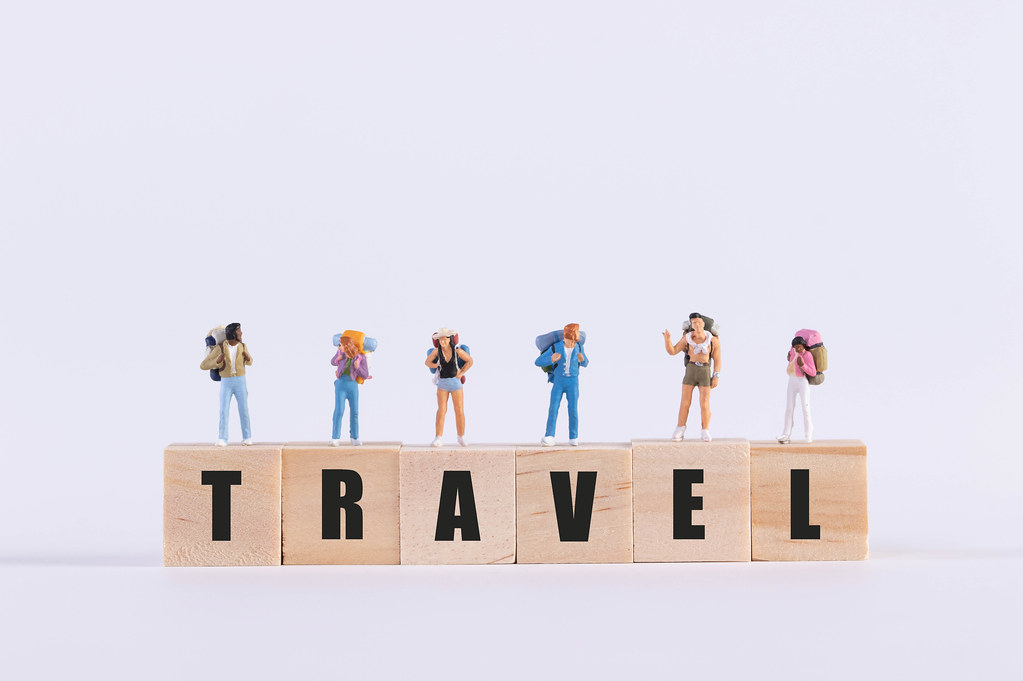Miniature travelers standing on wooden cubes with Travel text
