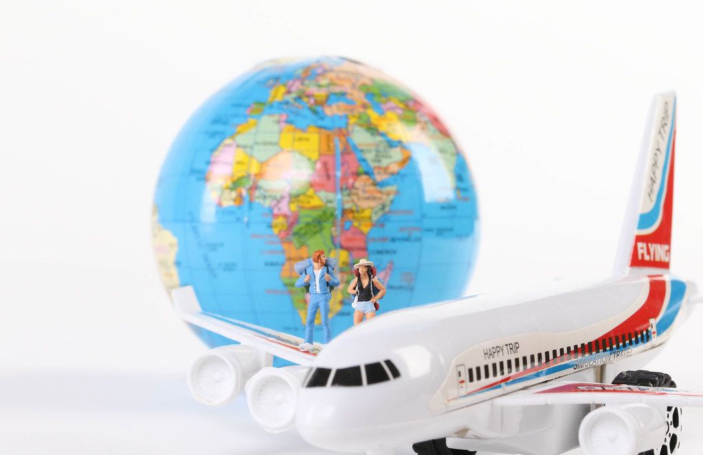 Miniature travelers with globe and airplane on white background
