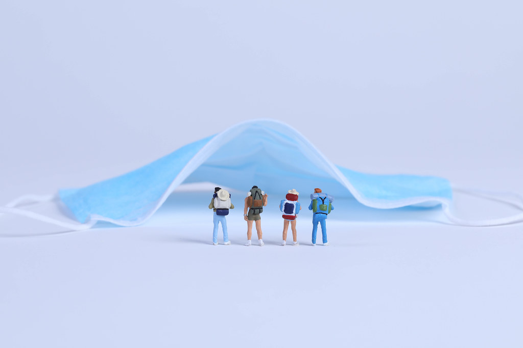 Miniature travelers with medical face mask on blue background