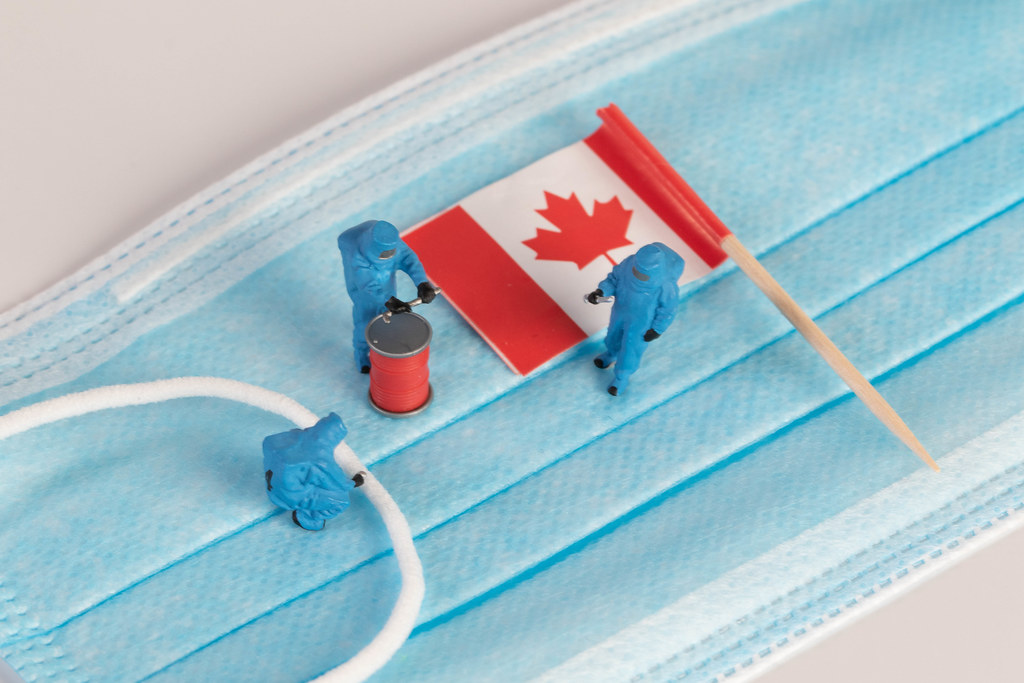 Miniature workers in protective clothes on a medical mask with flag of Canada